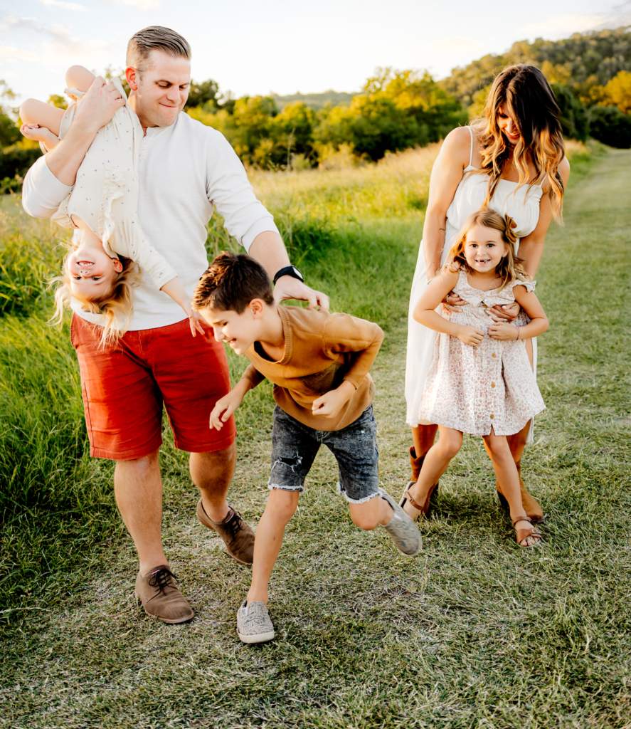 A joyful family laughing and playing together by the Colorado River at Common Ford Ranch Park during their photo session.