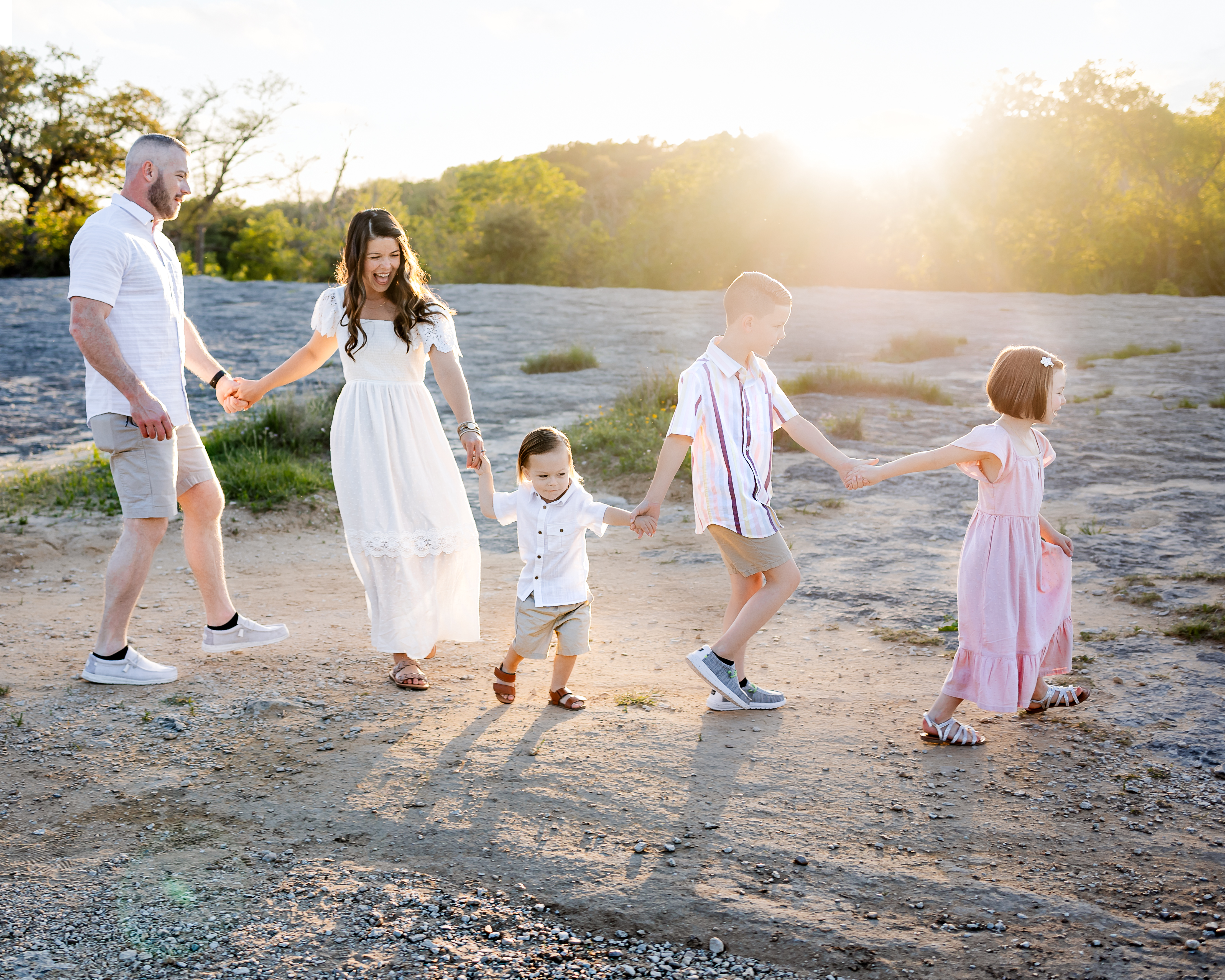 A family walking in a zig zag holding hands with children leading at Mckinney Falls state park.
