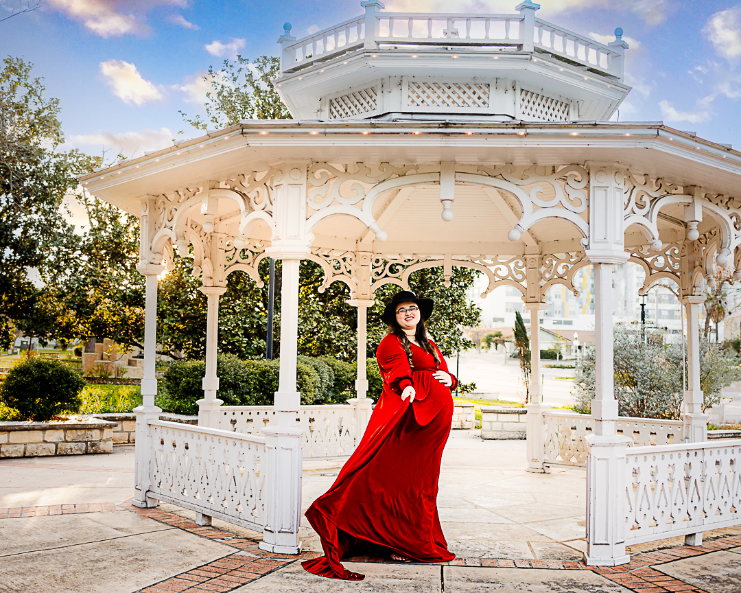 A pregnant mother wearing a red dress standing under a white gazebo.