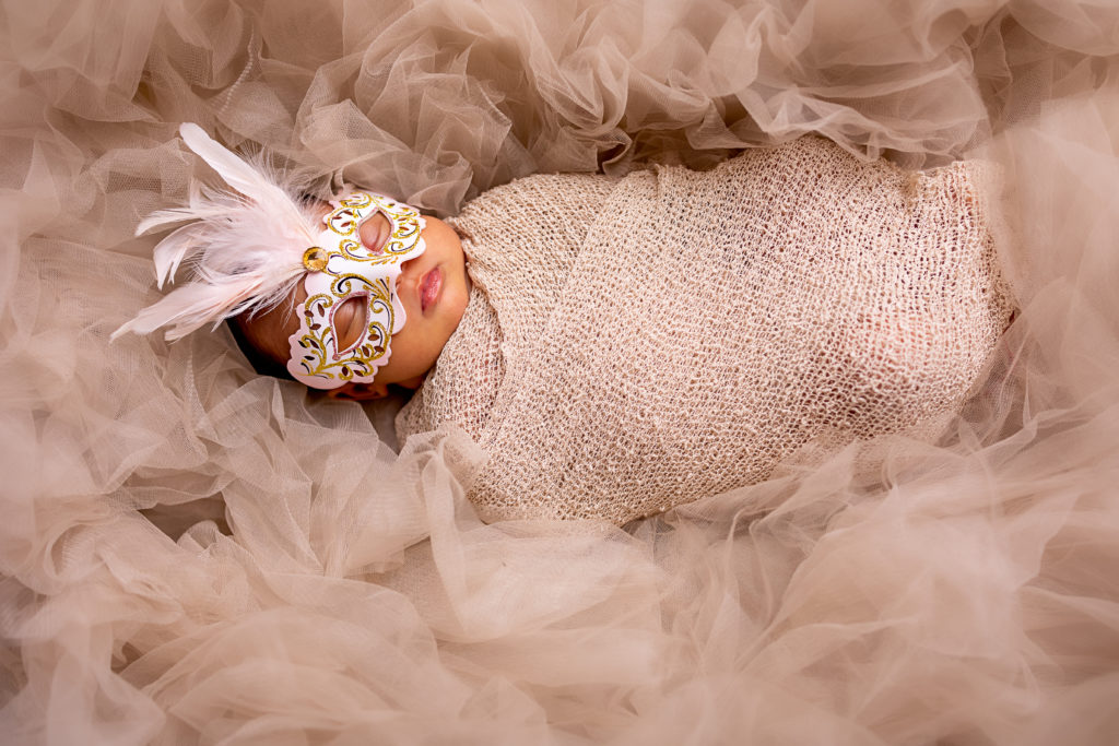 A beautiful newborn baby girl lying in tulle with a mask.