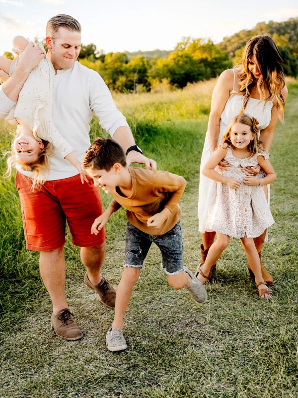 A joyful family laughing and playing together by the Colorado River at Common Ford Ranch Park during their photo session.